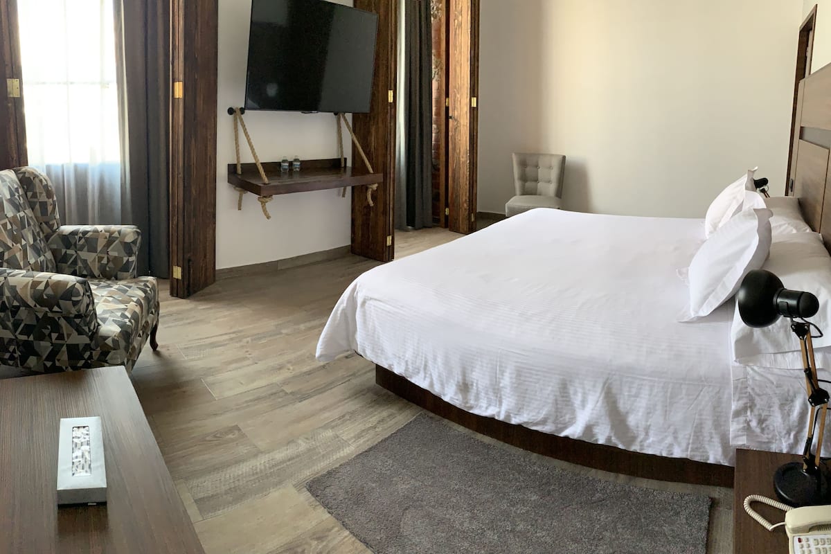 A hotel room with a bed, a chair, a desk, a TV, and a phone.