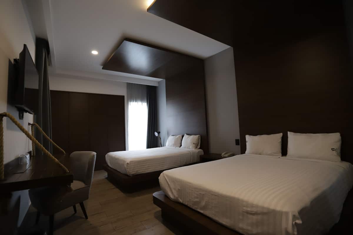 A hotel room with two beds, a desk, a chair, a large mirror, and a window with curtains.