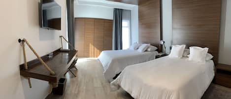 A hotel room with two beds, a TV mounted on the wall, a desk with a chair, and a wooden wardrobe.