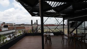 A rooftop terrace with a view of a cityscape, including a church tower, and a covered seating area with tables and chairs.