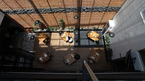 Vue d’ensemble d’un restaurant avec de nombreuses tables et chaises, un mur en briques et des lampes suspendues.