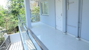 Ein sauberer, moderner Balkon mit Glasgeländer, einer weißen Tür und einem Fenster.