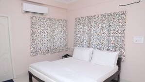 Ein Schlafzimmer mit einem Bett, floralen Vorhängen, einer Klimaanlage und einem Nachttisch.