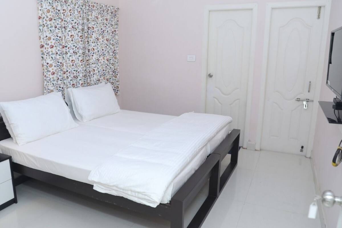 A neatly made bed with white linens, a bedside table with a phone, and a wall-mounted TV.