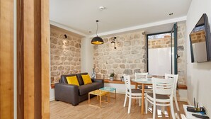 Un salon chaleureux avec un mur en pierre, un canapé agrémenté de coussins jaunes, une table à manger avec des chaises et une petite table basse.
