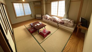 A traditional Japanese-style room with tatami flooring, a low table with cushions, a sofa, and a television on a wooden stand.