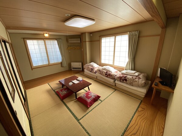 A traditional Japanese-style room with tatami flooring, a low table with cushions, a sofa, and a television on a wooden stand. - Nozawa Dream Central (Nozawaonsen)
