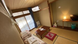 A traditional Japanese room with tatami flooring, a futon bed, a wooden table, a television, and a shoji screen.