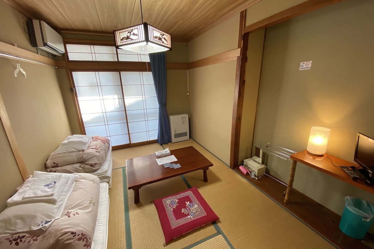 Een traditionele Japanse kamer met tatami vloerbedekking, een futon bed, een houten tafel, een bureau met lamp en schuifdeuren van shoji papier.