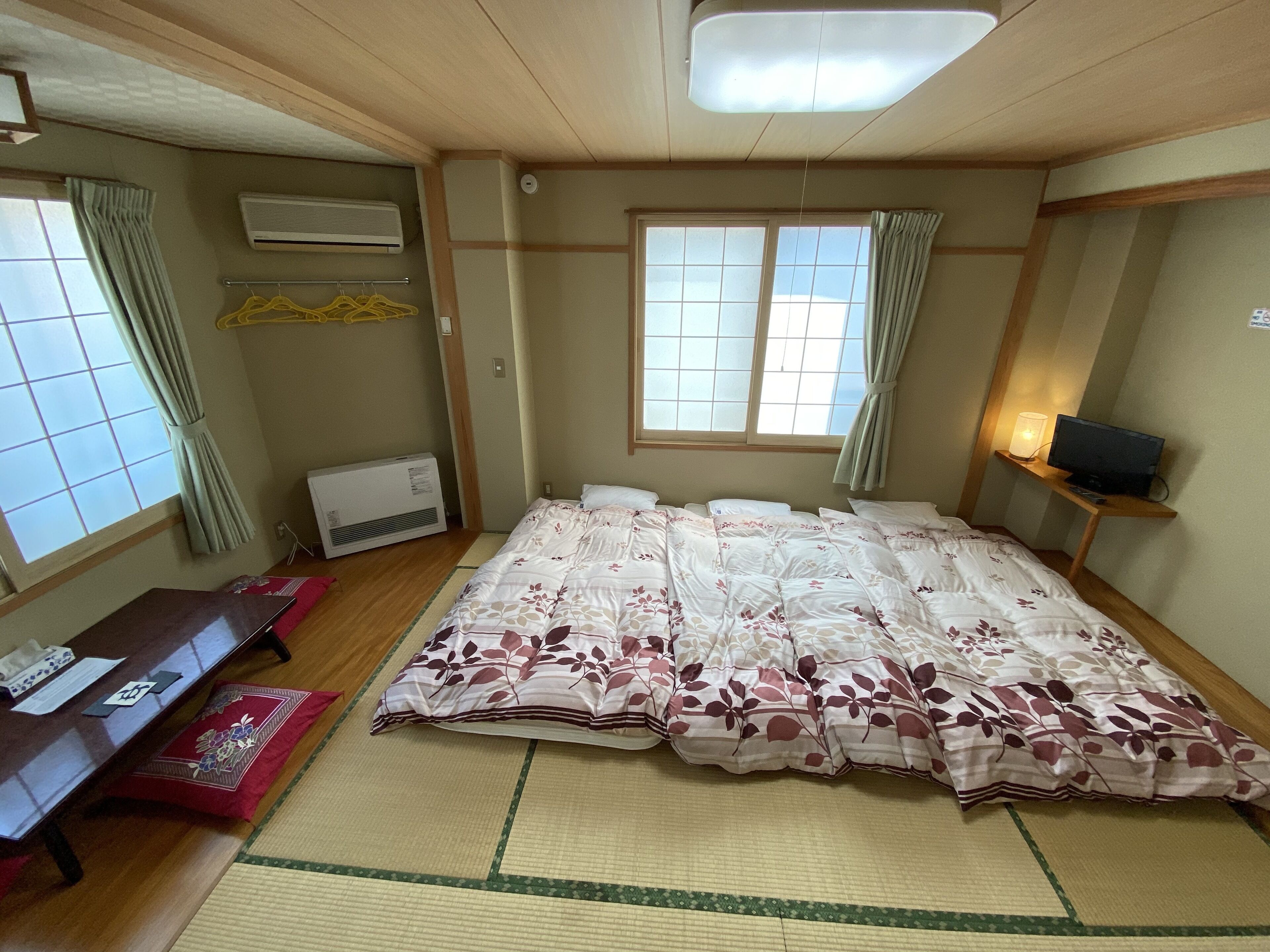 A room with a bed, a desk, an air conditioner, and a window with curtains.