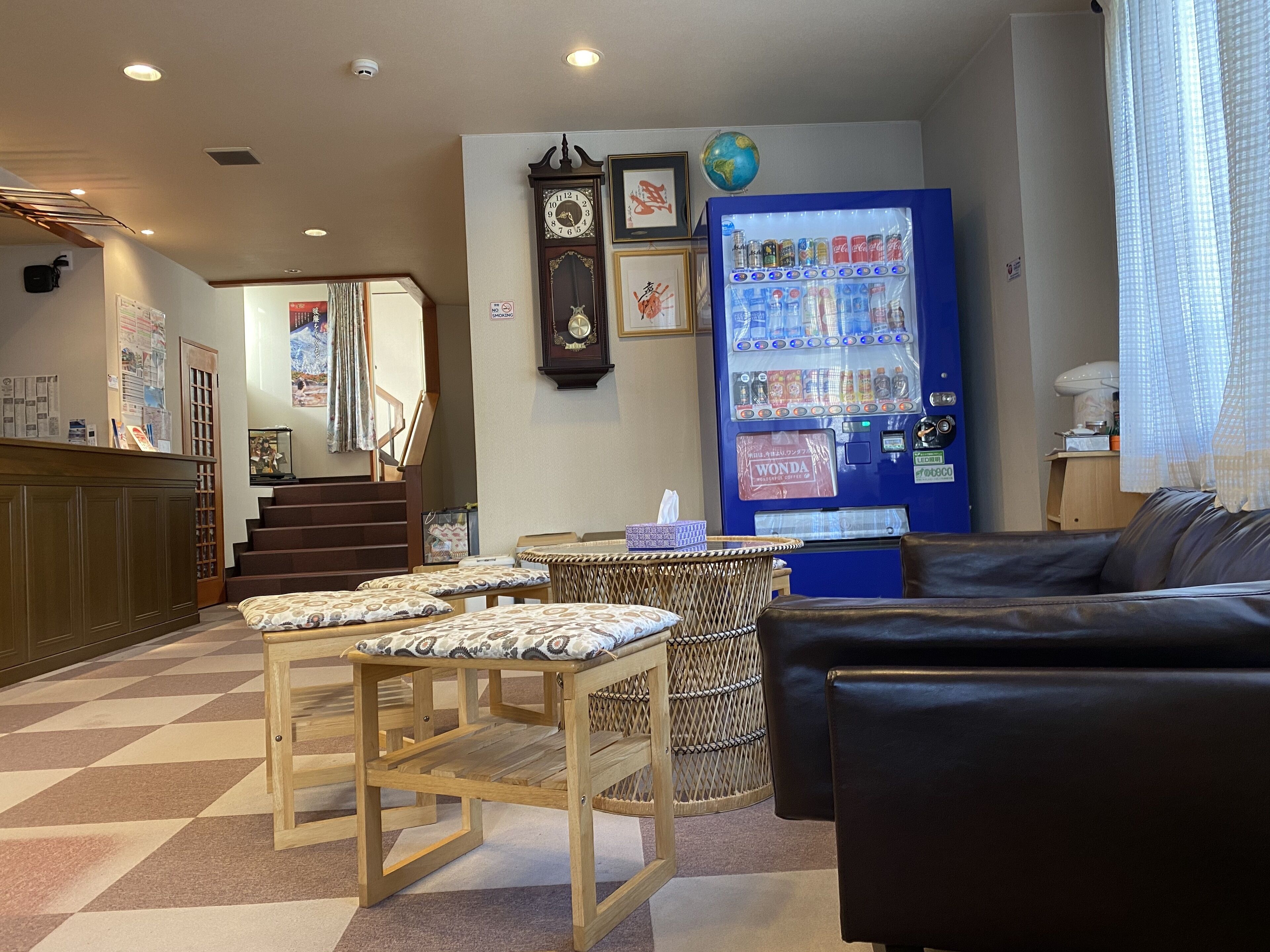 A hotel lobby with a checkered floor, a reception desk, a clock, a vending machine, and seating areas.