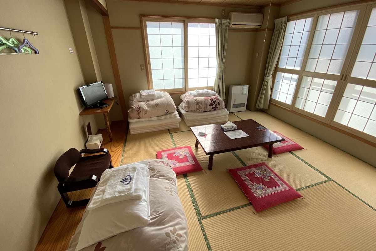 Een traditionele Japanse kamer met tatami vloeren, een futonbed, een klein bureau met een computer en een schuifdeur.