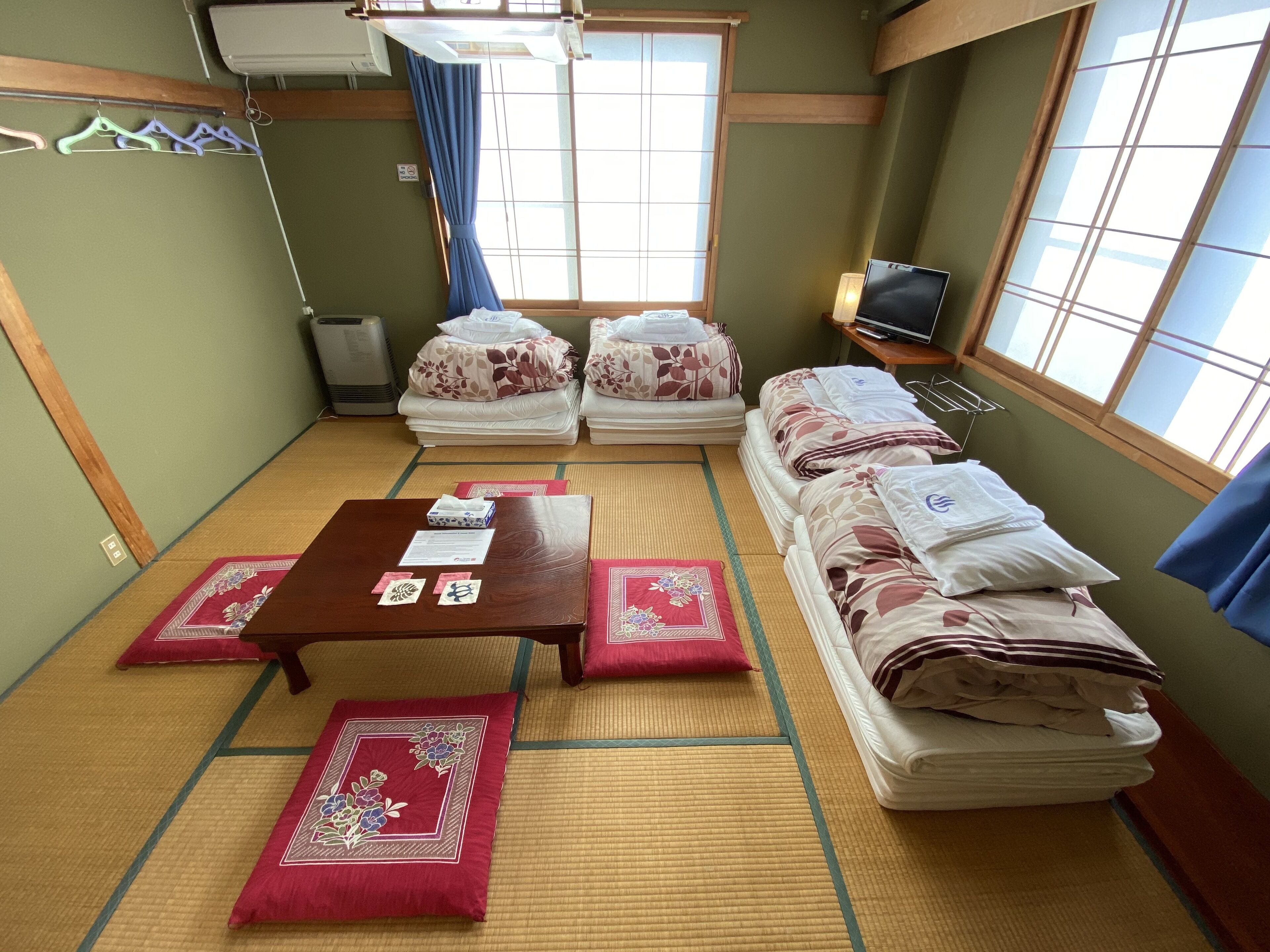 Una habitación japonesa tradicional con suelo de tatami, camas futón, una mesita con una caja de pañuelos y un televisor sobre un mueble.