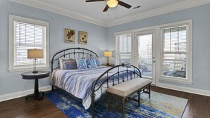 Quarto com cama, um banquinho, ventilador de teto e duas luminárias de cabeceira.