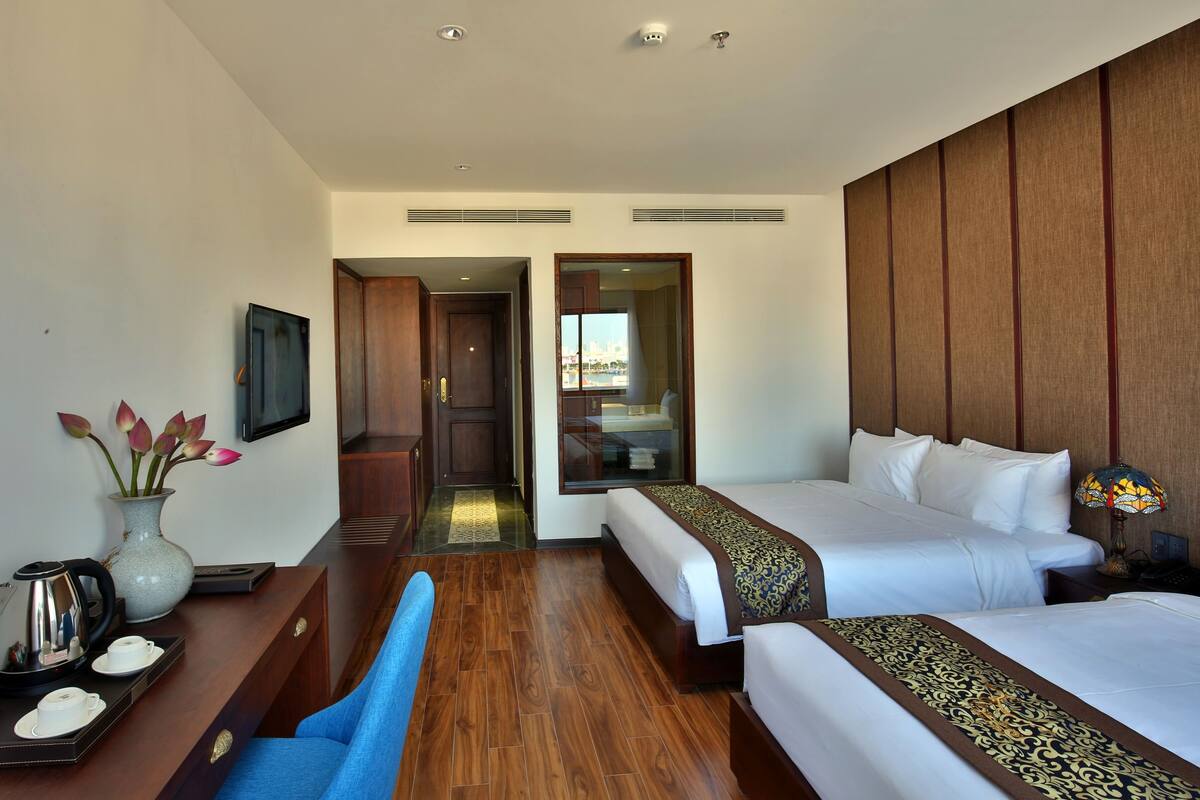 A hotel room with two beds, a desk with a coffee maker, and a vase with flowers.