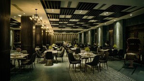A modern restaurant interior with high ceilings, patterned ceiling, and elegant chandeliers. Tables are arranged in a spacious layout with dark chairs. - Dong Duong Hotel (Da Nang)