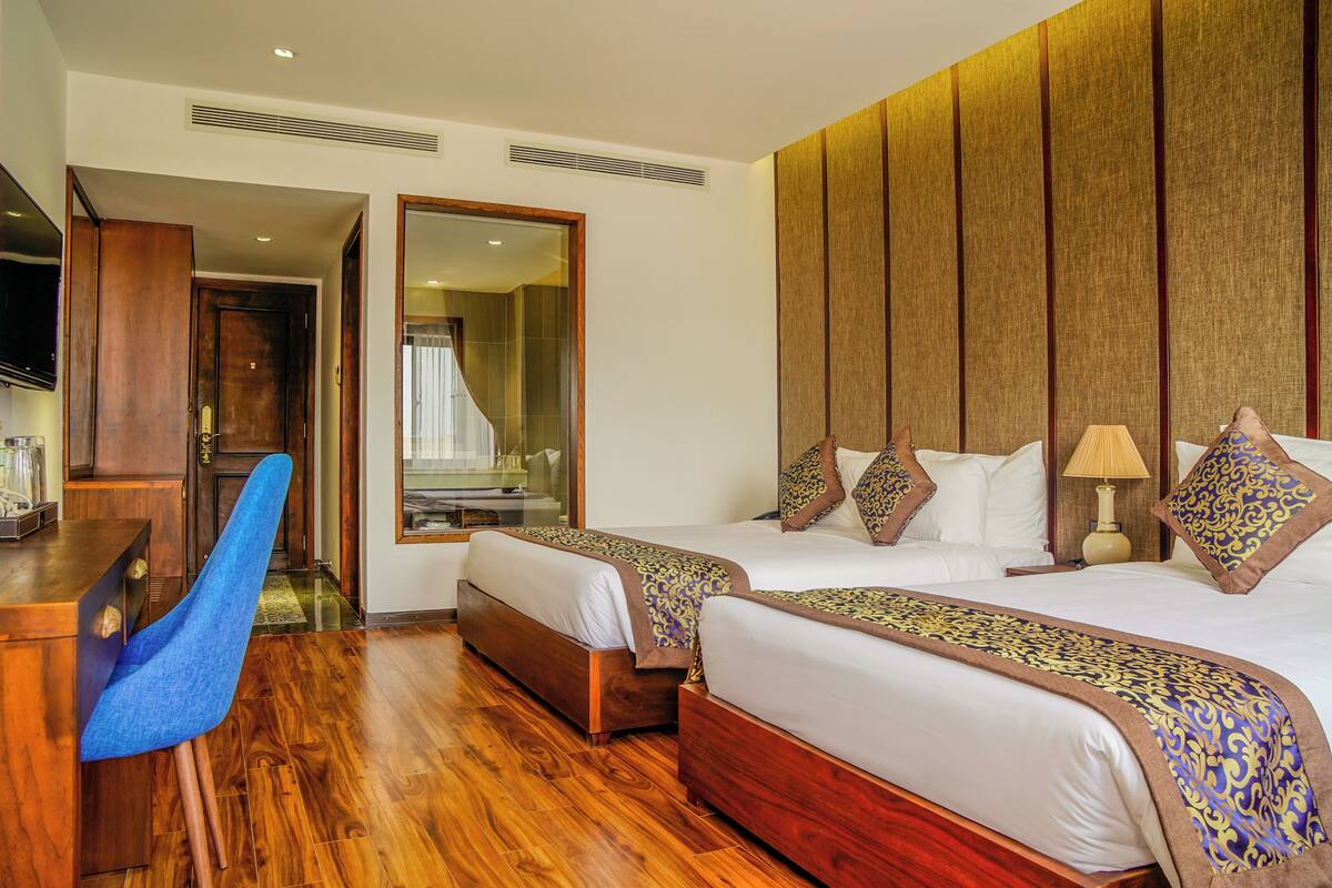 A hotel room with two beds, a wooden desk, a blue chair, and a large mirror.
