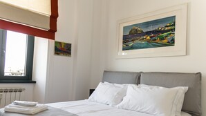 A neatly made bed with white linens, a window with blinds, and two framed artworks on the wall. - Bright, stylish, renovated Flat near Villa Borghese (Roma)