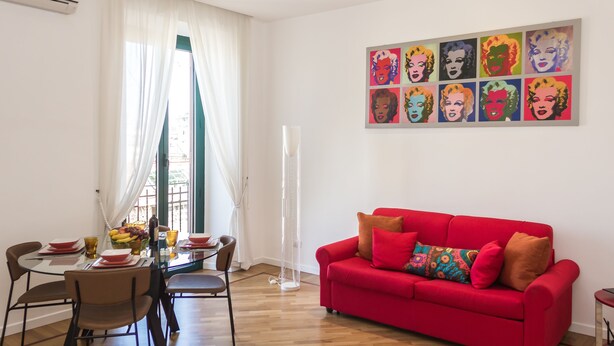 A modern living room with a red sofa, a dining table with chairs, and a large window with sheer curtains. - Bright, stylish, renovated Flat near Villa Borghese (Roma)