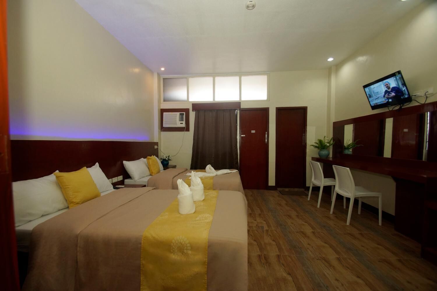 A hotel room with two beds, a desk, a TV, and a seating area.