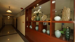 A hallway with a wooden display case containing various vases and a mirror. - Hacasi Hotel (Tacloban)
