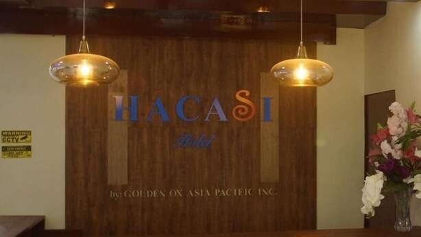 A reception desk with a wooden backdrop displaying the name "HACASI Hotel" and the logo "GOLDEN OX ASIA PACIFIC INC." - Hacasi Hotel (Tacloban)