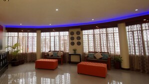 A spacious living room with a large TV, multiple seating areas, and large windows with curtains. - Hacasi Hotel (Tacloban)