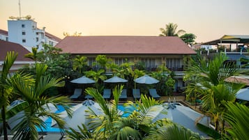 A hotel with a swimming pool surrounded by palm trees and lounge chairs.