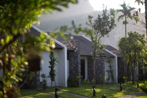 A traditional-style building with stone and white walls, surrounded by a well-maintained garden with pathways and small trees. - Aravinda Resort (Nam Hoa Lu)