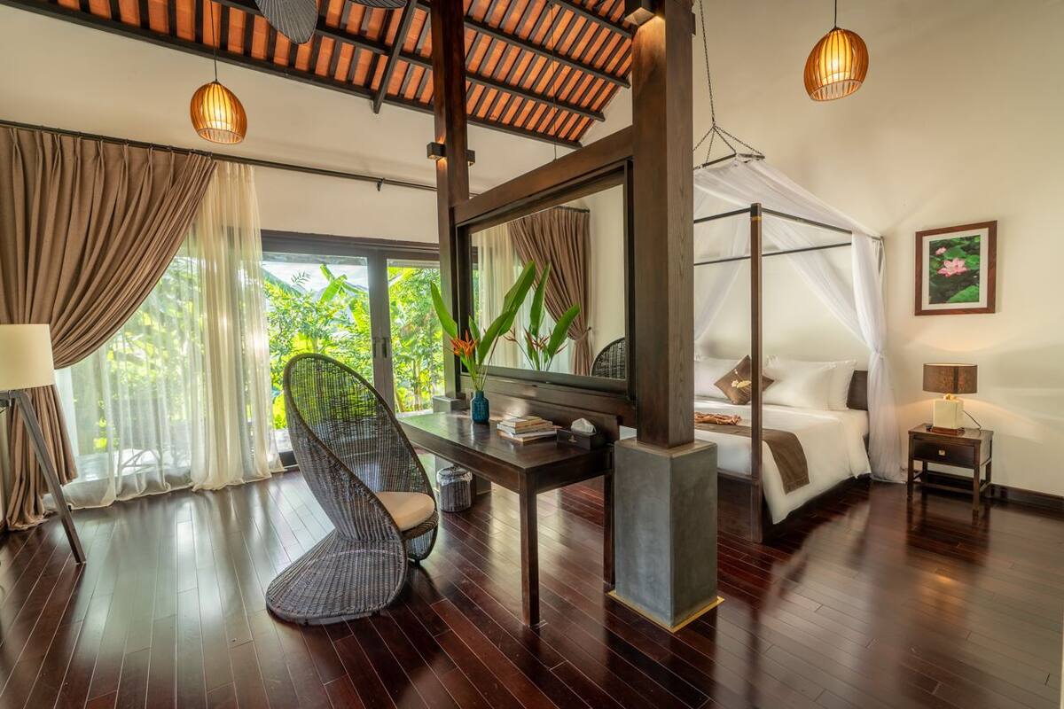 A modern bedroom with a canopy bed, a large mirror, a wicker chair, and a view of greenery outside.