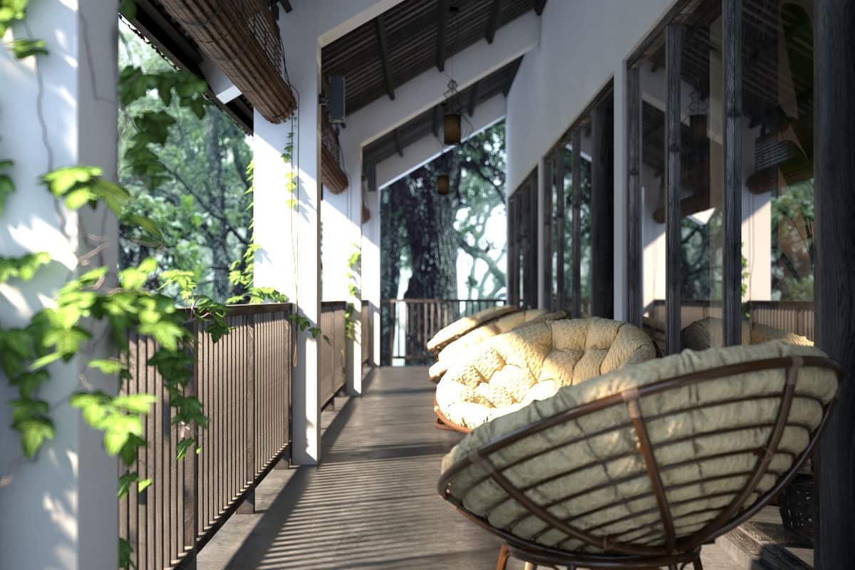 A covered outdoor area with a wooden floor, a large wicker chair, and a view of a tree through the glass wall.