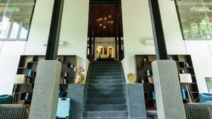 A spacious lobby with a high ceiling, a staircase leading to upper floors, and a modern design with minimalistic furniture. - Aravinda Resort (Nam Hoa Lu)