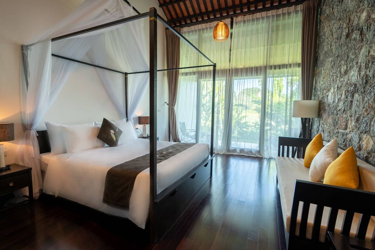 A four-poster bed with a canopy, a sofa with cushions, a nightstand, and a lamp.