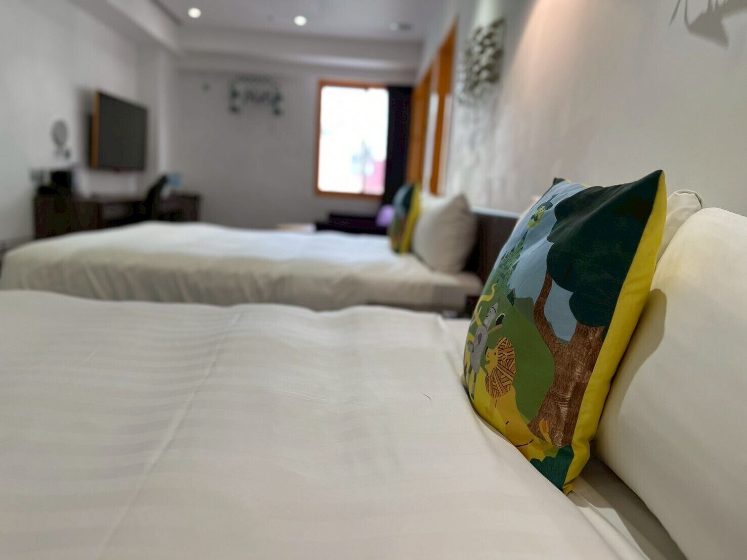 A hotel room with two beds, a TV on the wall, and a window with curtains.