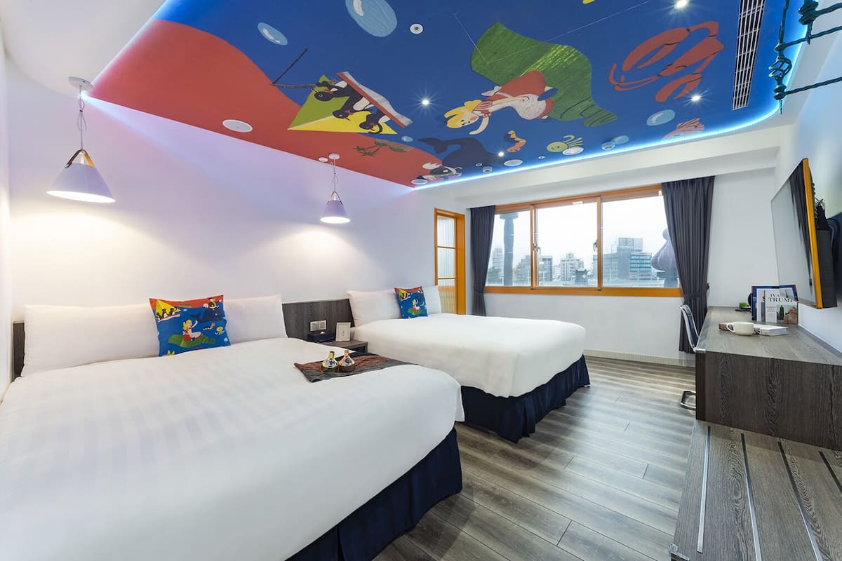 A hotel room with two beds, a city view, a desk, and a ceiling mural.