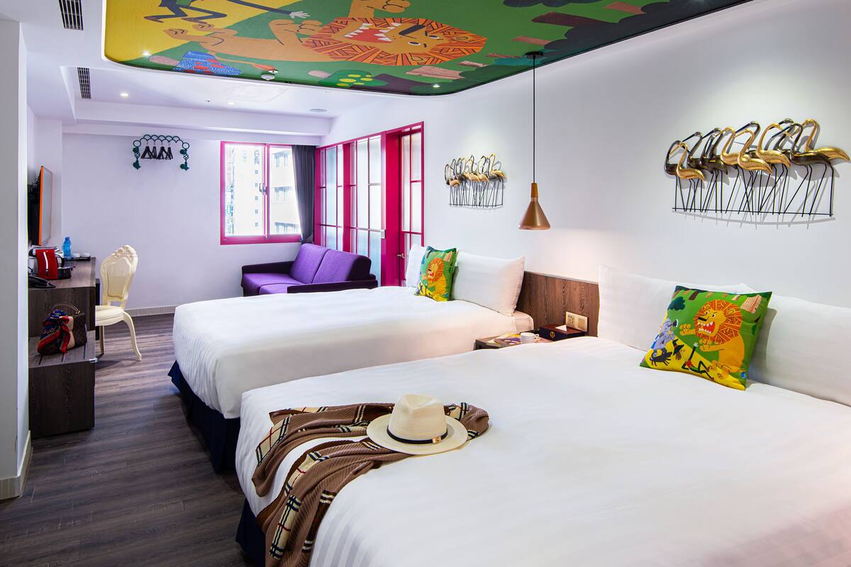 A hotel room with two beds, a desk, a chair, and a colorful ceiling mural.