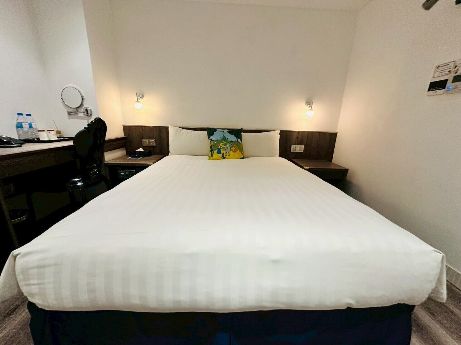 A hotel room with a large bed, a desk with a chair, a small table, and two bedside tables with lamps.
