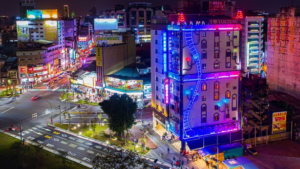 Een fel verlicht hotel met een opvallende trap en neonborden.