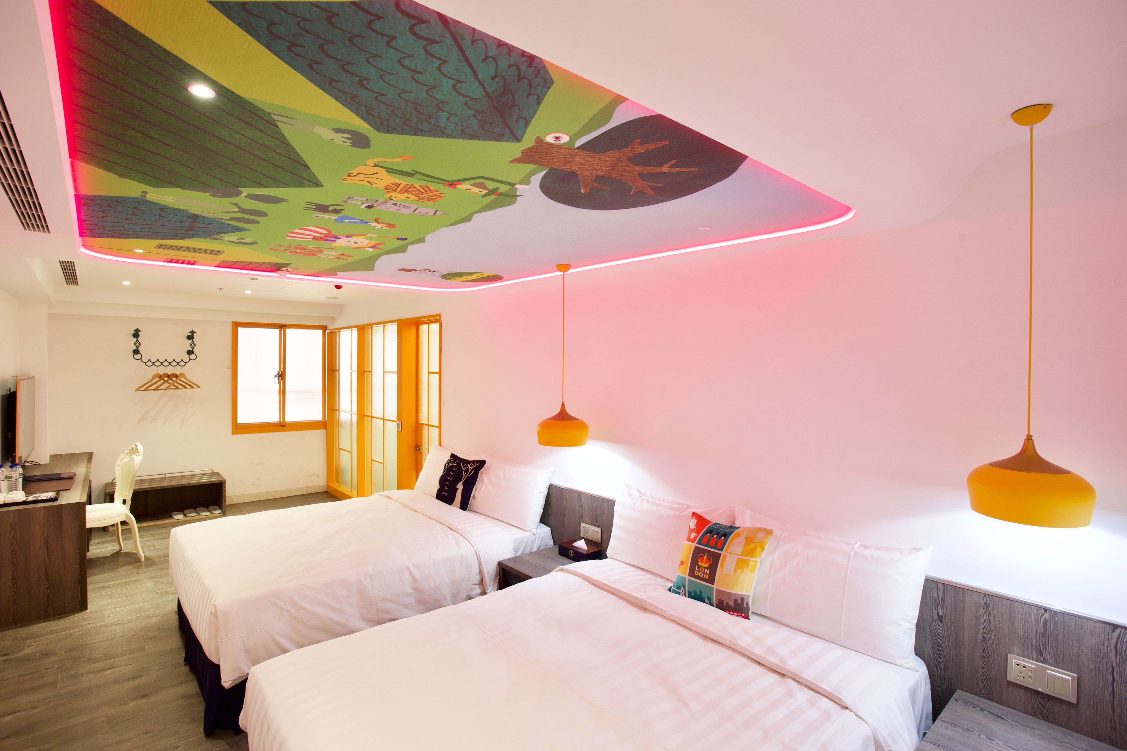 A hotel room with two beds, a desk, a chair, and a ceiling mural.
