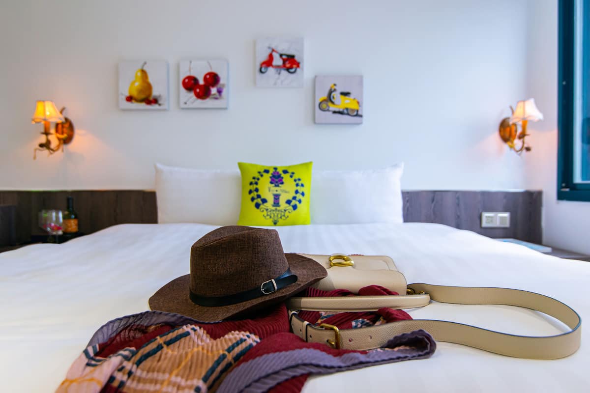 A bed with a hat, a handbag, and a blanket. There are wall art pieces and wall sconces.
