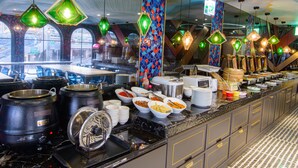 Een buffetopstelling met diverse soorten eten en bakken, een patroonplafond en hangende groene lampen.