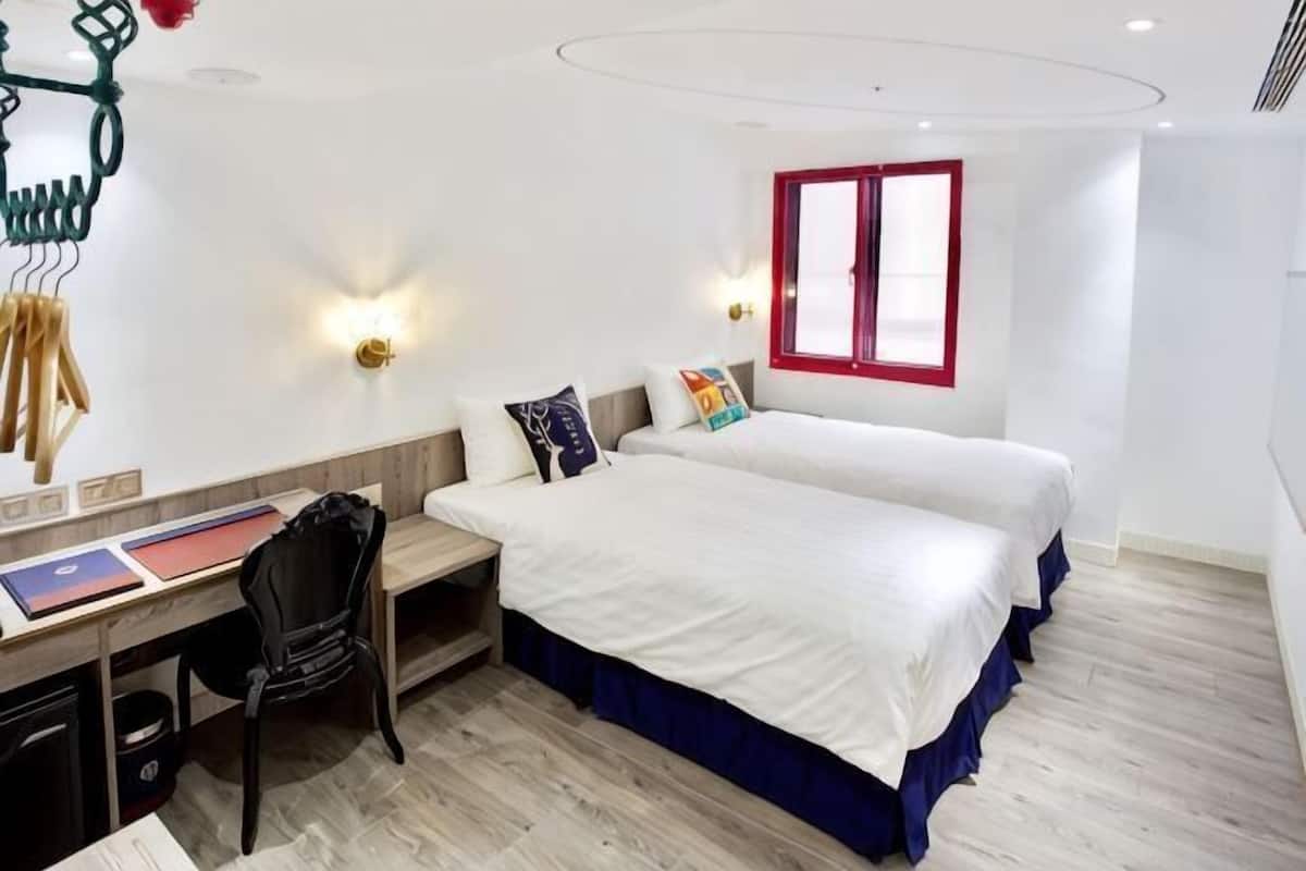 A bedroom with two beds, a desk, and a chair.