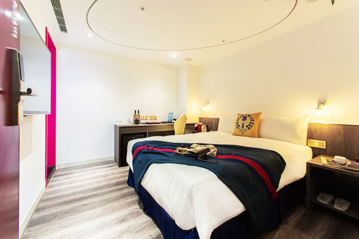 A hotel room with a bed, bedside table, desk, and a chair.