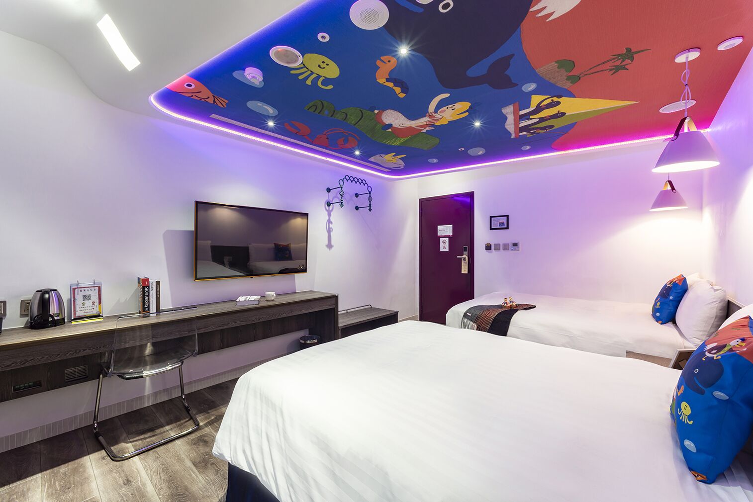 A hotel room with a large bed, a smaller bed, a desk with a flat-screen TV, a mirror, and a ceiling mural with sea creatures.