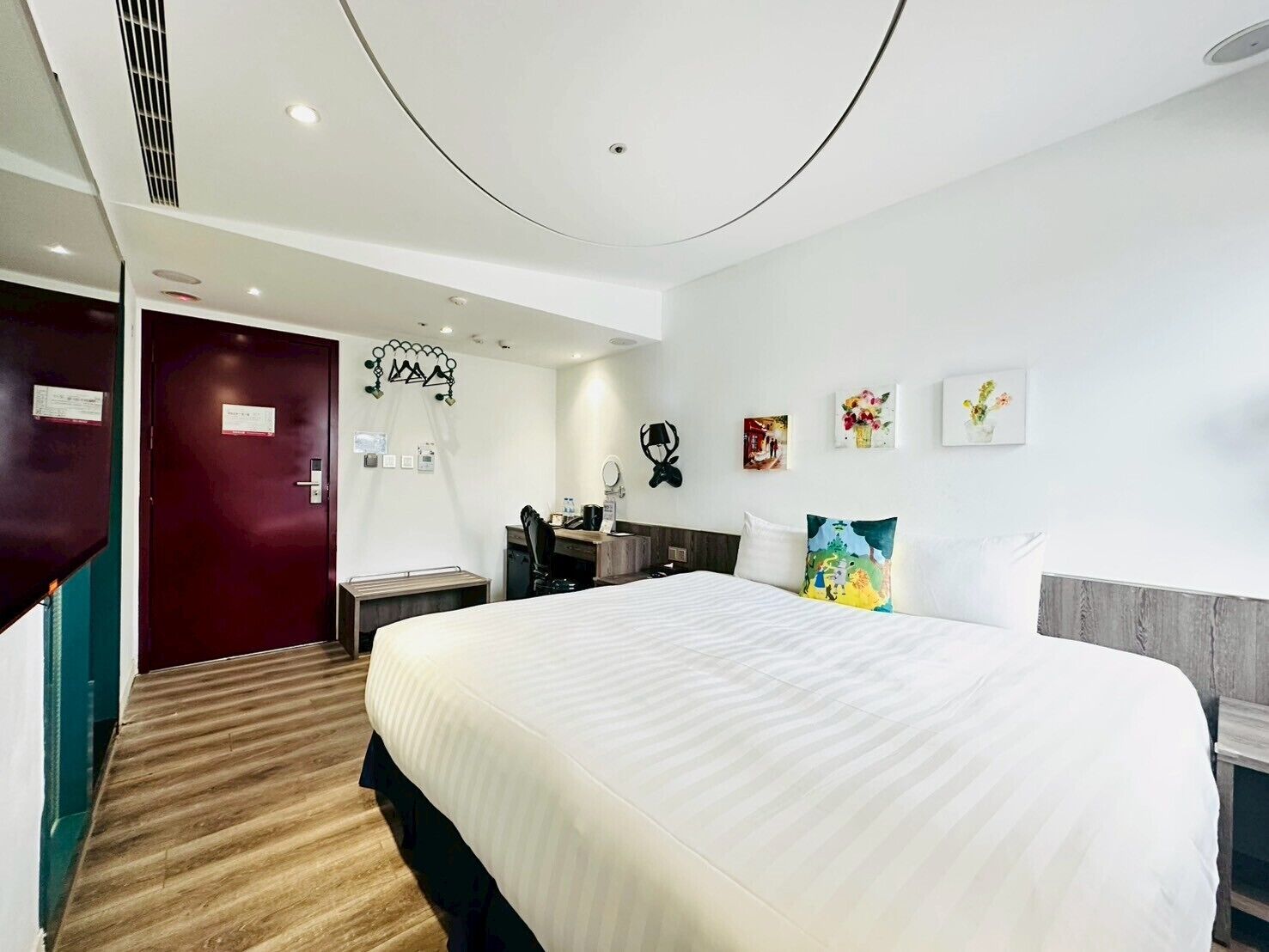 A hotel room with a large bed, a desk, a chair, and a small desk lamp.