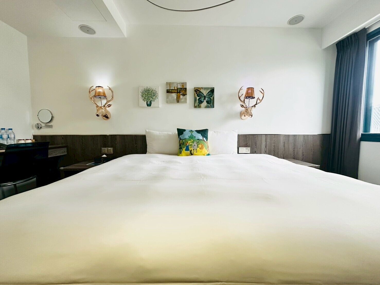 Habitación de hotel con una cama grande, un escritorio, una silla, un espejo y decoración en la pared, incluyendo una cabeza de venado y obras de arte enmarcadas.