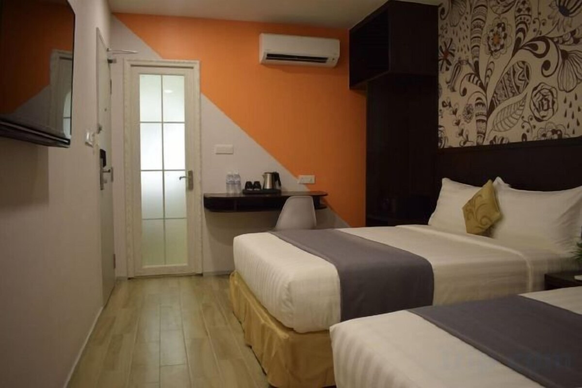 A hotel room with two beds, a desk, and an air conditioning unit.