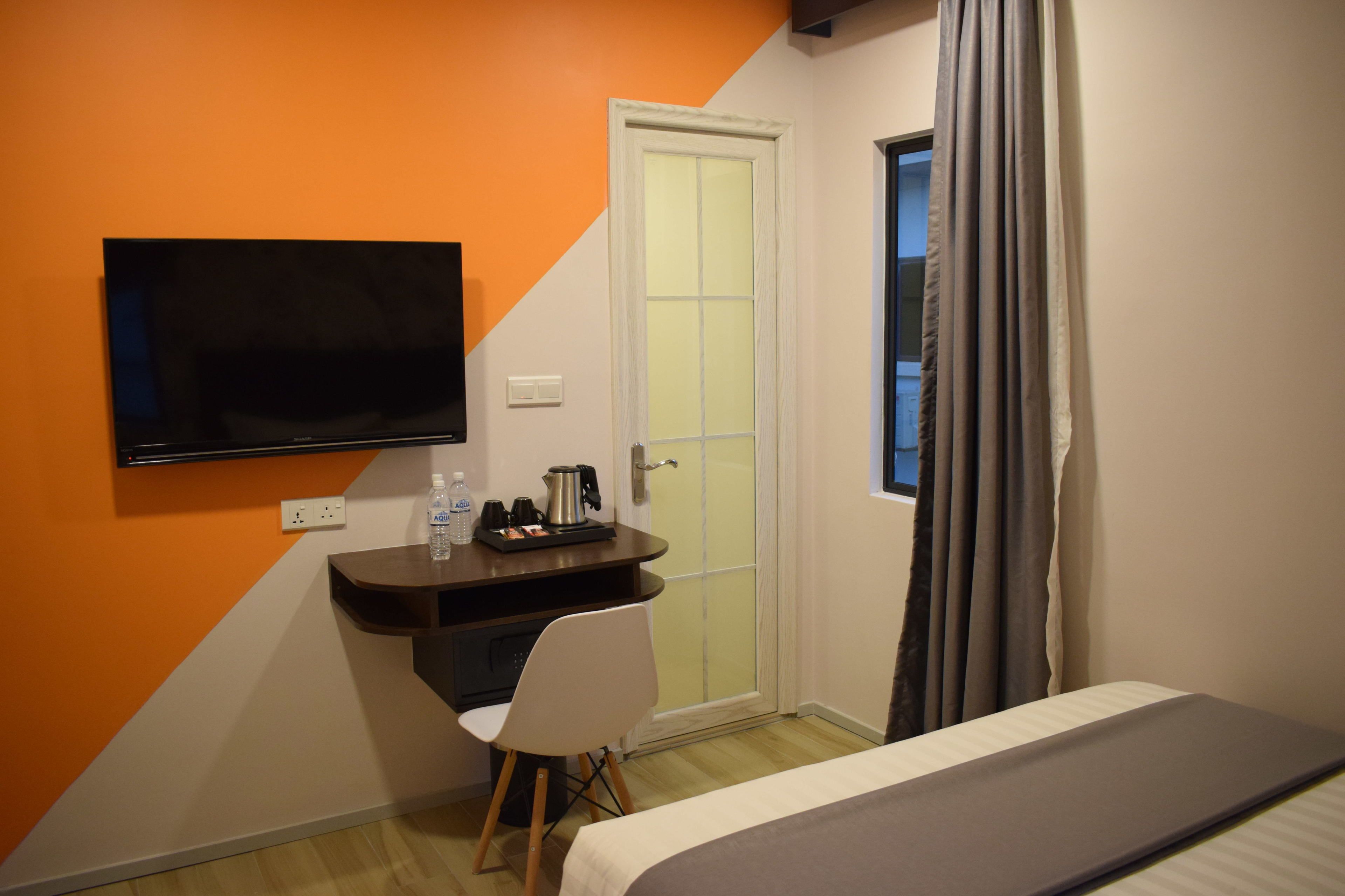 Ein Hotelzimmer mit einem Bett, einem Schreibtisch mit Stuhl, einem an der Wand befestigten Fernseher und einem Fenster mit Vorhängen.