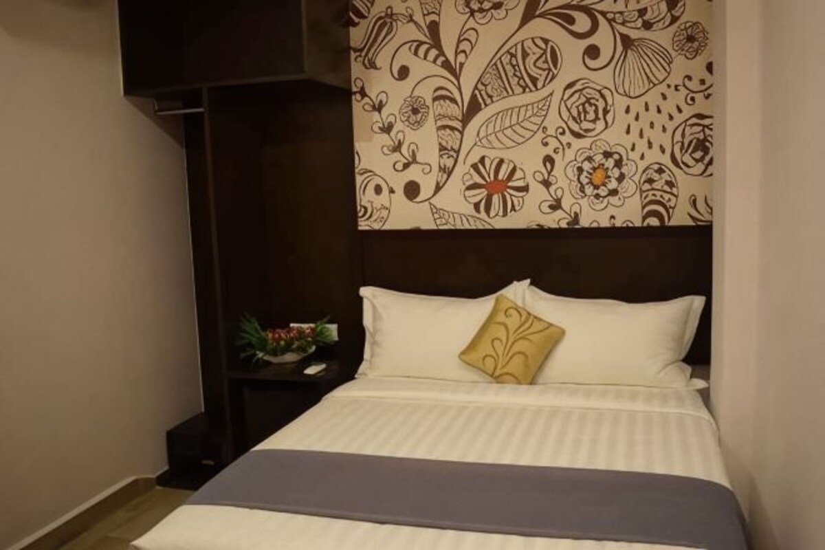 A bed with a patterned headboard, a bedside table with a plant, and a wall with a floral design.