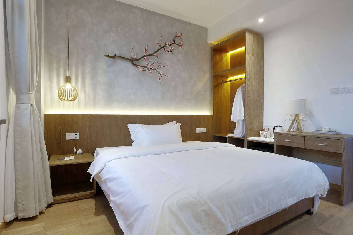 Une chambre d’hôtel moderne avec un grand lit, des tables de chevet en bois, une décoration murale en forme de branche et une table de chevet avec une lampe.